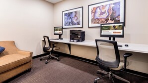 A conference room with two monitors, a printer, a desk, and a cushioned chair.