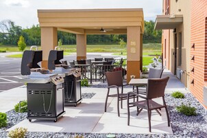 An outdoor patio with barbecue grills, seating, and a brick building in the background.