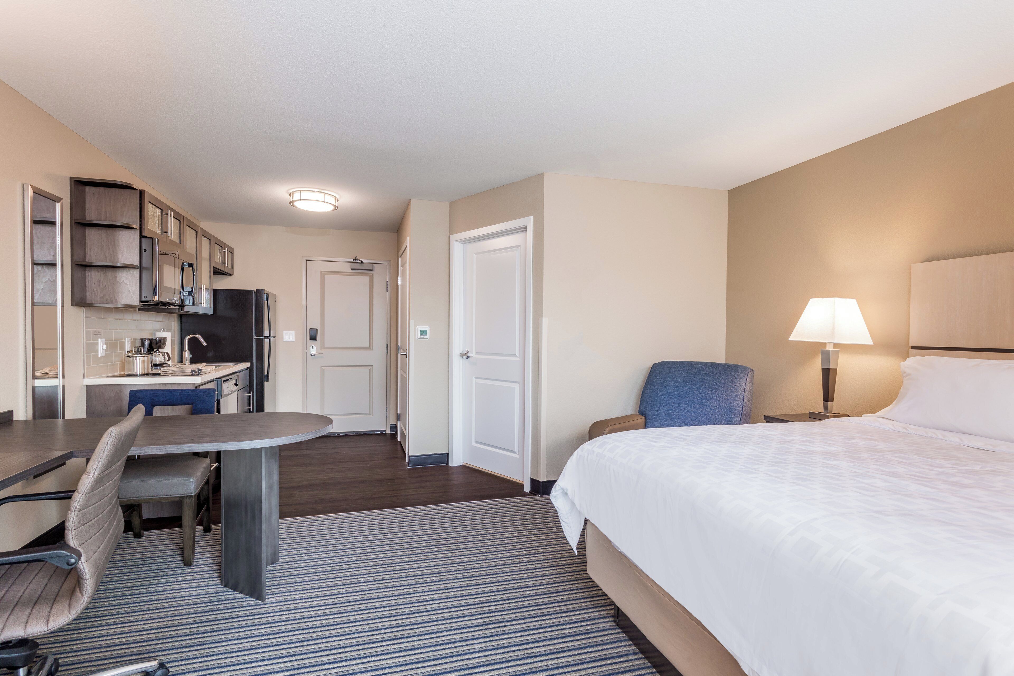 A hotel room with a bed, a desk with a chair, a kitchenette, and a bathroom.