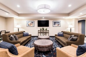 A hotel lobby with two sofas, a coffee table, a flat-screen TV, and a small table with plants. - Candlewood Suites Eau Claire I-94 by IHG (Eau Claire)