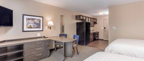 Una habitación de hotel con cama, escritorio con silla, kitchenette pequeño y televisor en la pared.