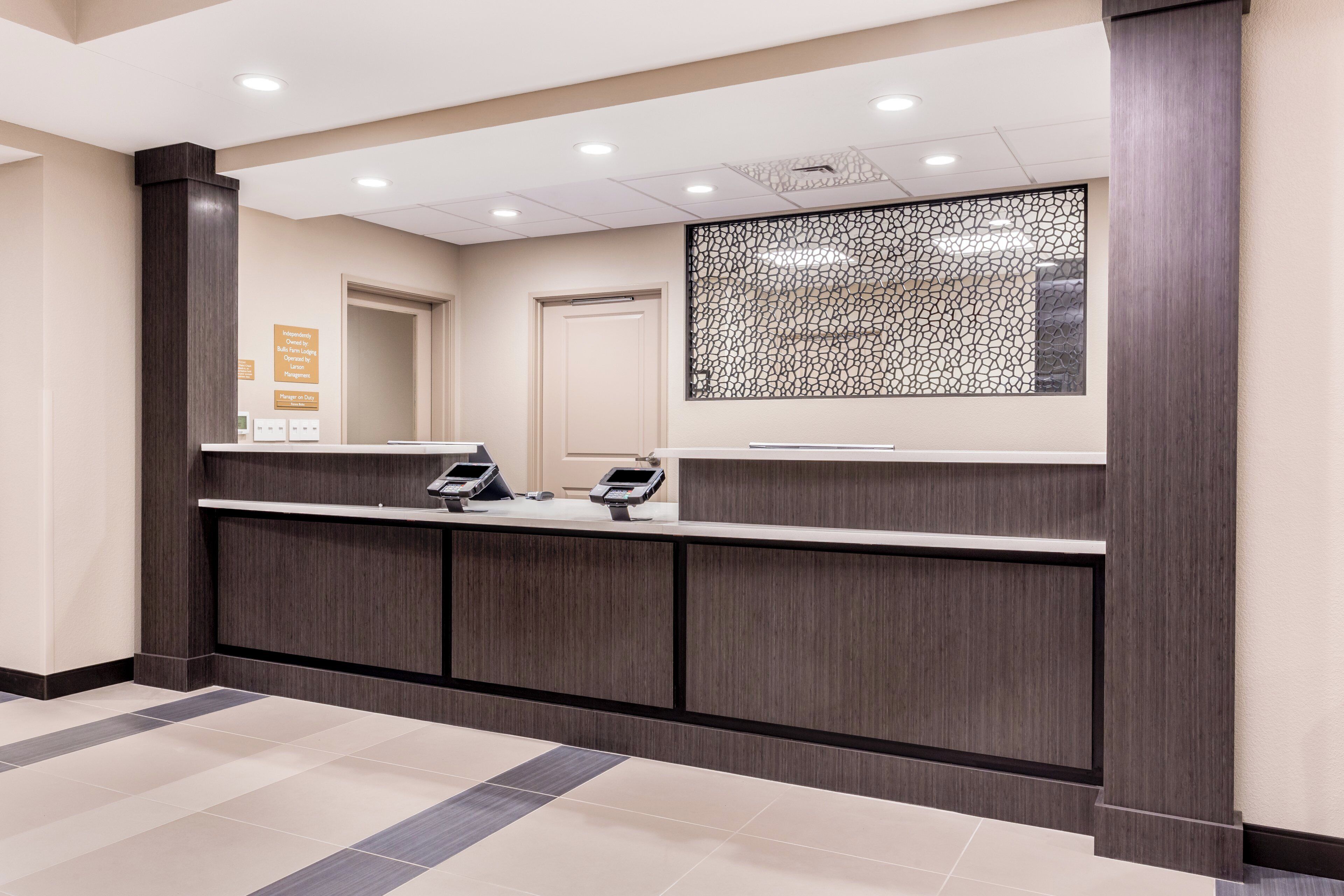 Zona de recepción con un mostrador de madera oscura, dos lectores de tarjetas, un panel decorativo y una puerta.