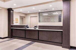 Zona de recepción con un mostrador de madera oscura, dos lectores de tarjetas, un panel decorativo y una puerta.