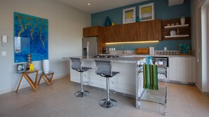 A modern kitchen with a central island, bar stools, and a decorative painting on the wall. - Designer Condo in Zona Romantica (Puerto Vallarta)