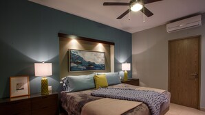 A bedroom with a bed, bedside lamps, a ceiling fan, an air conditioner, and a door. - Designer Condo in Zona Romantica (Puerto Vallarta)