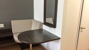 A small room with a round table, a white chair, a mirror, and a door.