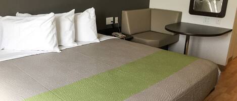 Habitación de hotel con cama, una silla, una mesita y un espejo en la pared.