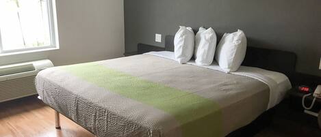 Een netjes opgemaakt bed met een gestreepte deken, een nachtkastje met een lamp en een raam met jaloezieën.