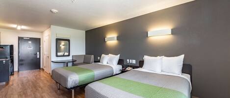 Une chambre d’hôtel avec deux lits, un bureau, un miroir et une kitchenette.