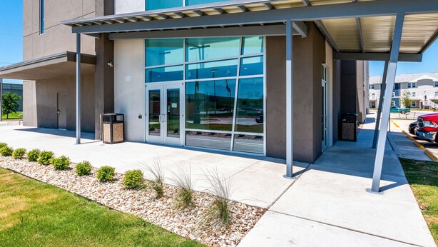 A modern building with large glass windows, a covered entrance, and a gravel pathway with small bushes. - Studio 6 San Marcos, TX (San Marcos)
