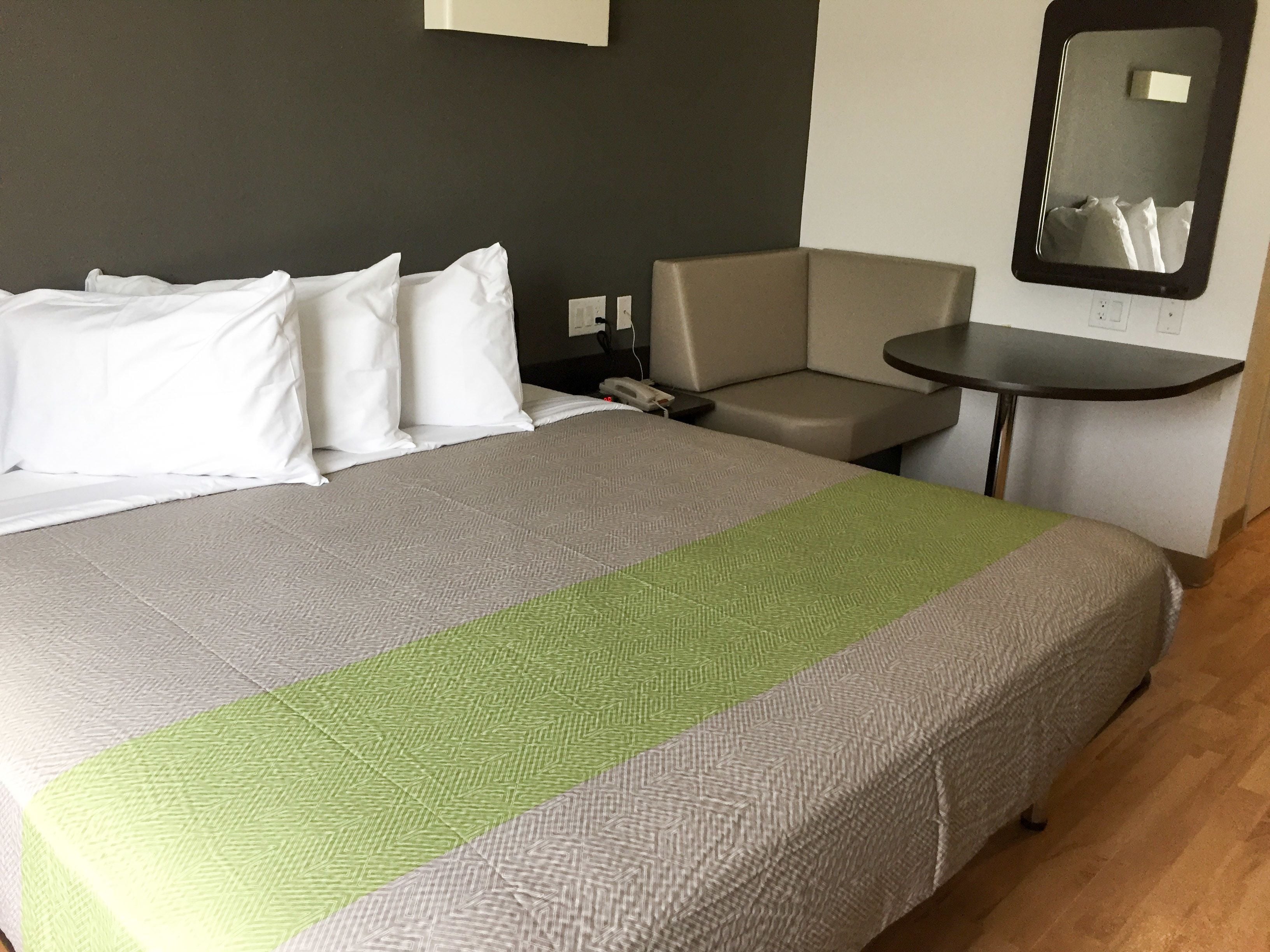 A hotel room with a large bed, a small table, a chair, and a mirror on the wall.
