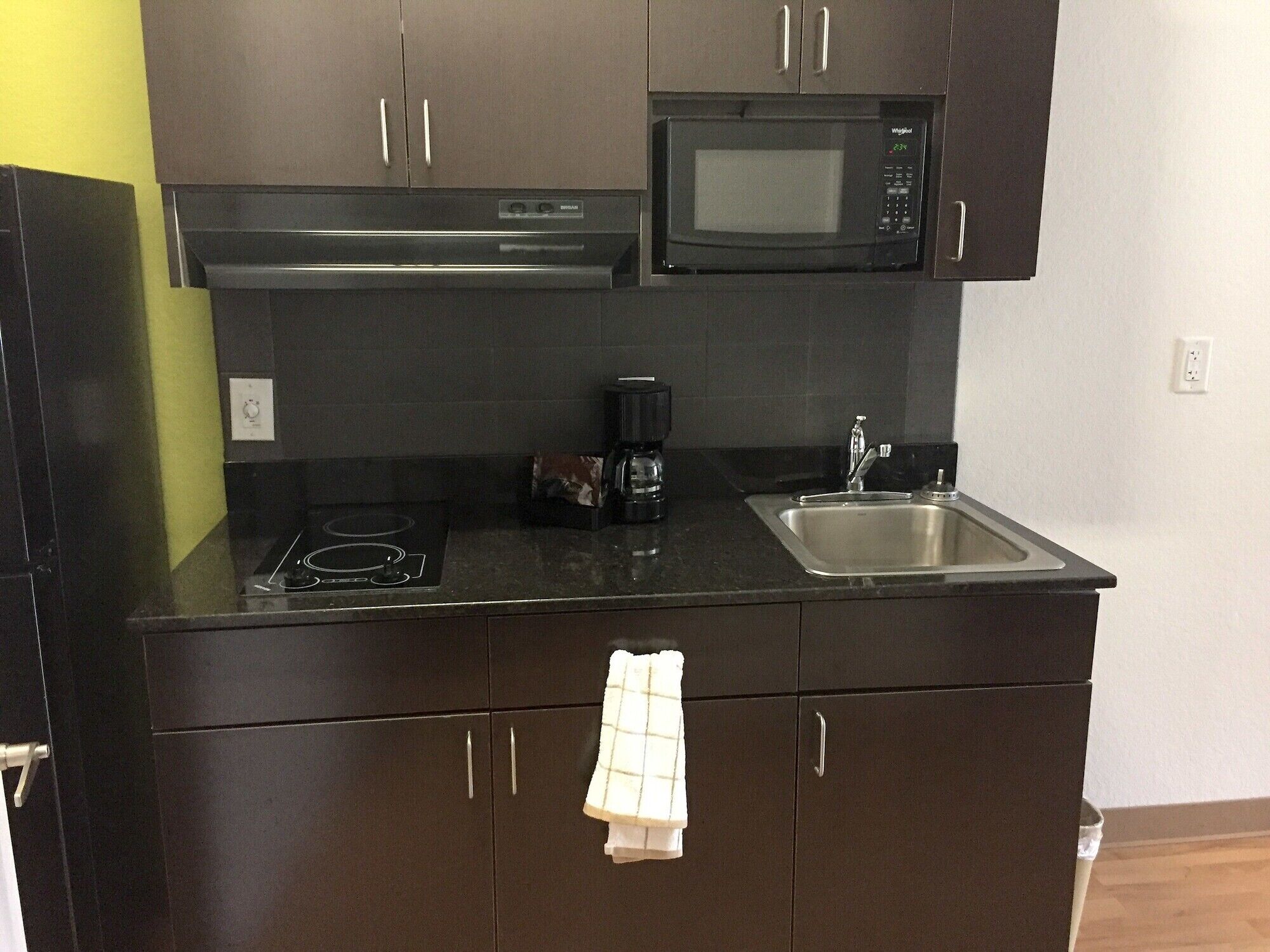 A kitchen with dark brown cabinets, a microwave, a stove, a sink, and a coffee maker.