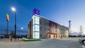 A multi-story hotel with a prominent '6' sign on the roof, large windows, and a parking lot with several vehicles. - Motel 6 Fort Worth, TX - North - Saginaw (Fort Worth)
