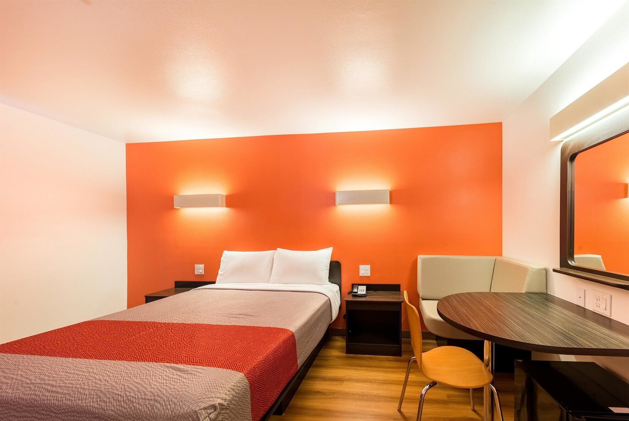 A hotel room with two beds, a small table, a chair, and a mirror.