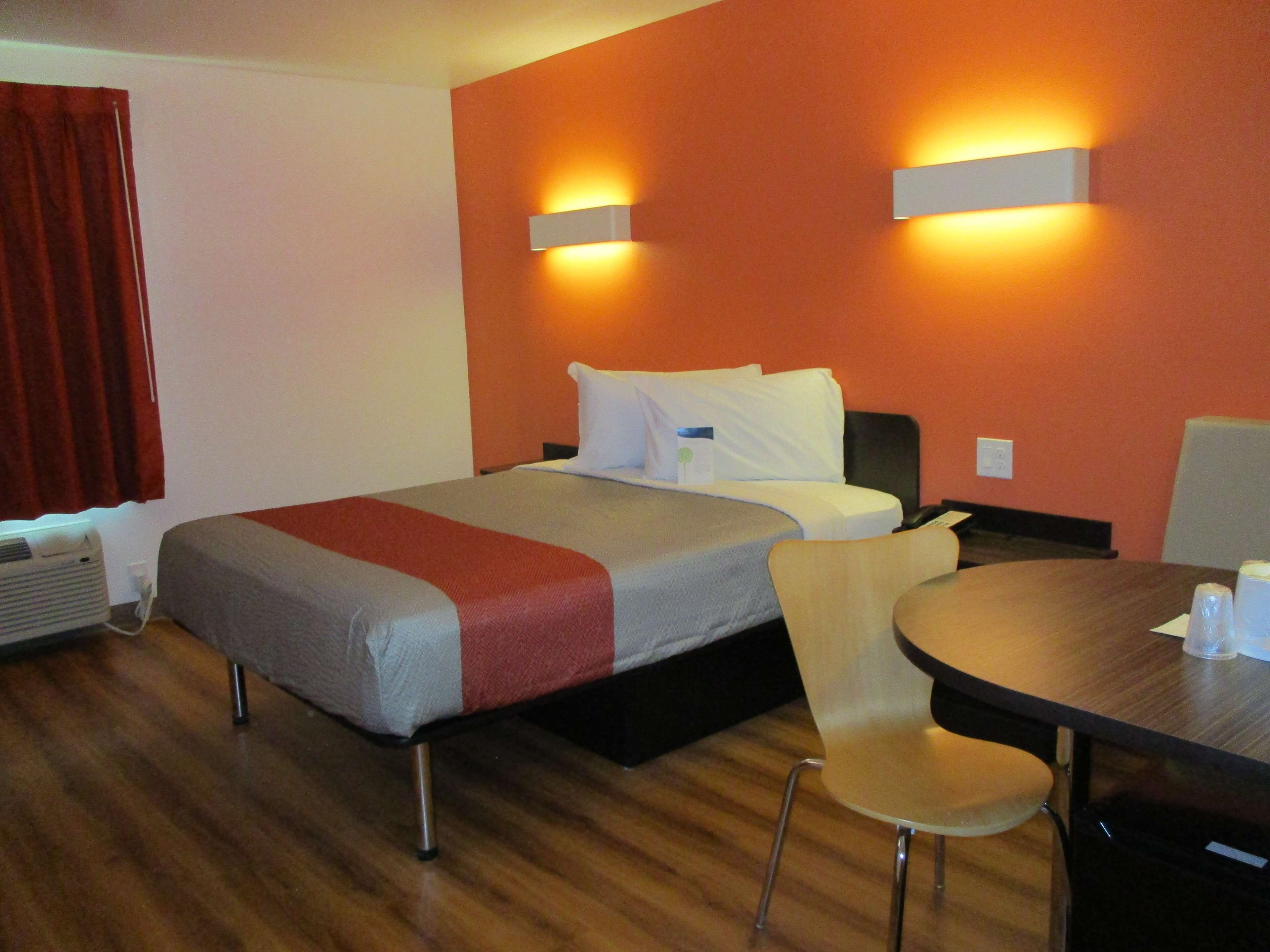 A hotel room with a bed, a chair, a table, and a wall-mounted heater.