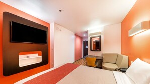 A hotel room with a bed, a TV mounted on the wall, a small table, a chair, and a mirror. - Motel 6 Fort Worth, TX - North - Saginaw (Fort Worth)