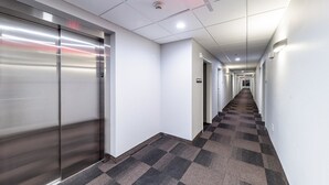 A hallway with a carpeted floor, a fire alarm, and a sign indicating a laundry room. - Motel 6 Fort Worth, TX - North - Saginaw (Fort Worth)
