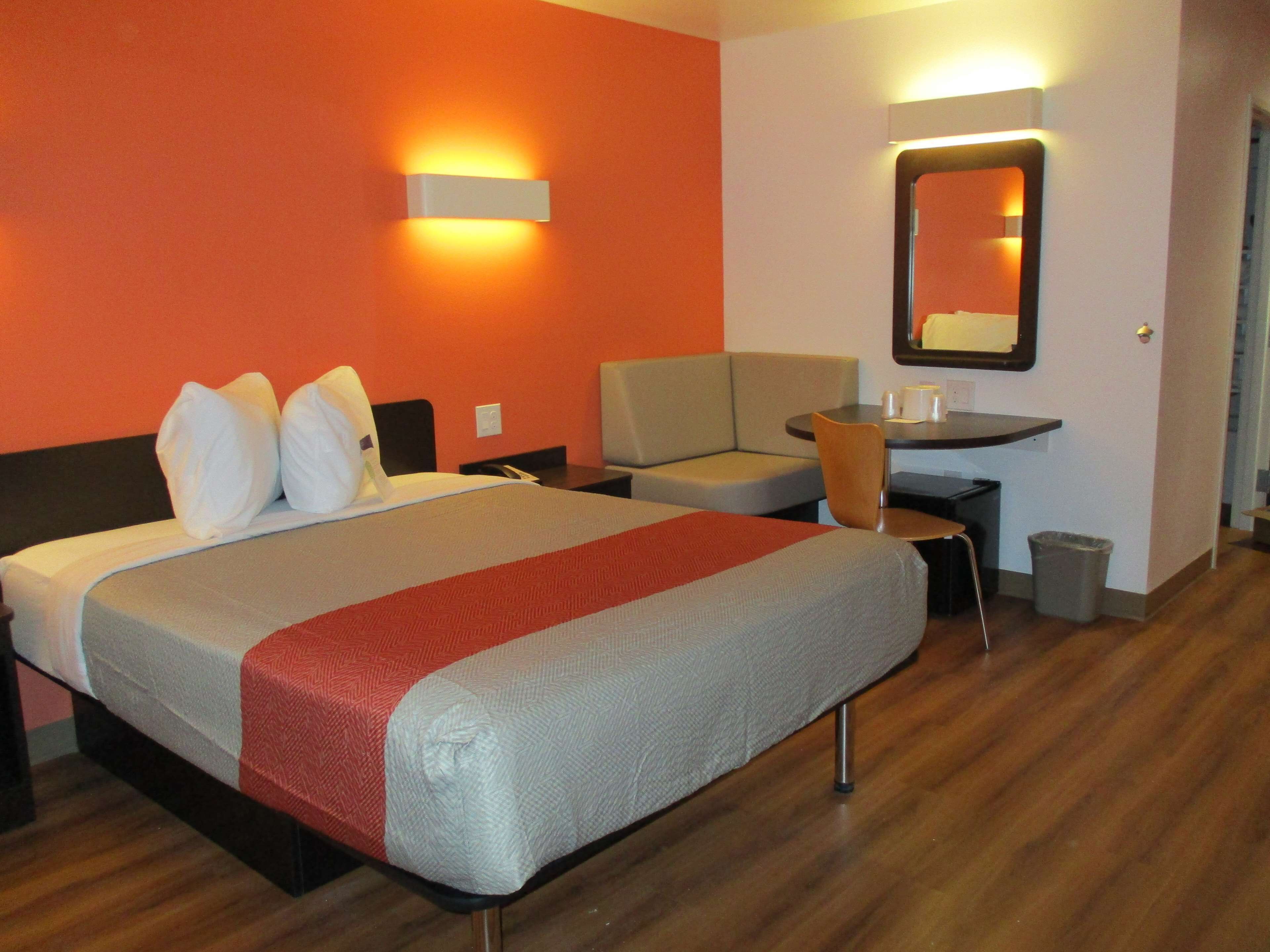 Une chambre d’hôtel avec un lit, un canapé, une petite table, une poubelle et un miroir.