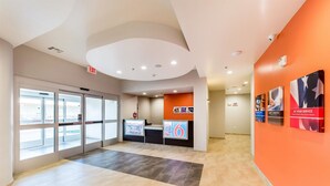 A hotel lobby with glass doors, a reception desk, and a digital display. - Motel 6 Fort Worth, TX - North - Saginaw (Fort Worth)