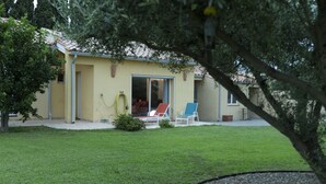 Una casa amb façana groga, un patio amb dues cadires i un arbre al primer pla.