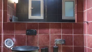 Een badkamer met een groot zwart wastafel, een spiegel en een wandlamp.