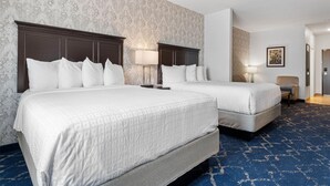 Habitación de hotel con dos camas, una silla, una lámpara y un cuadro en la pared.