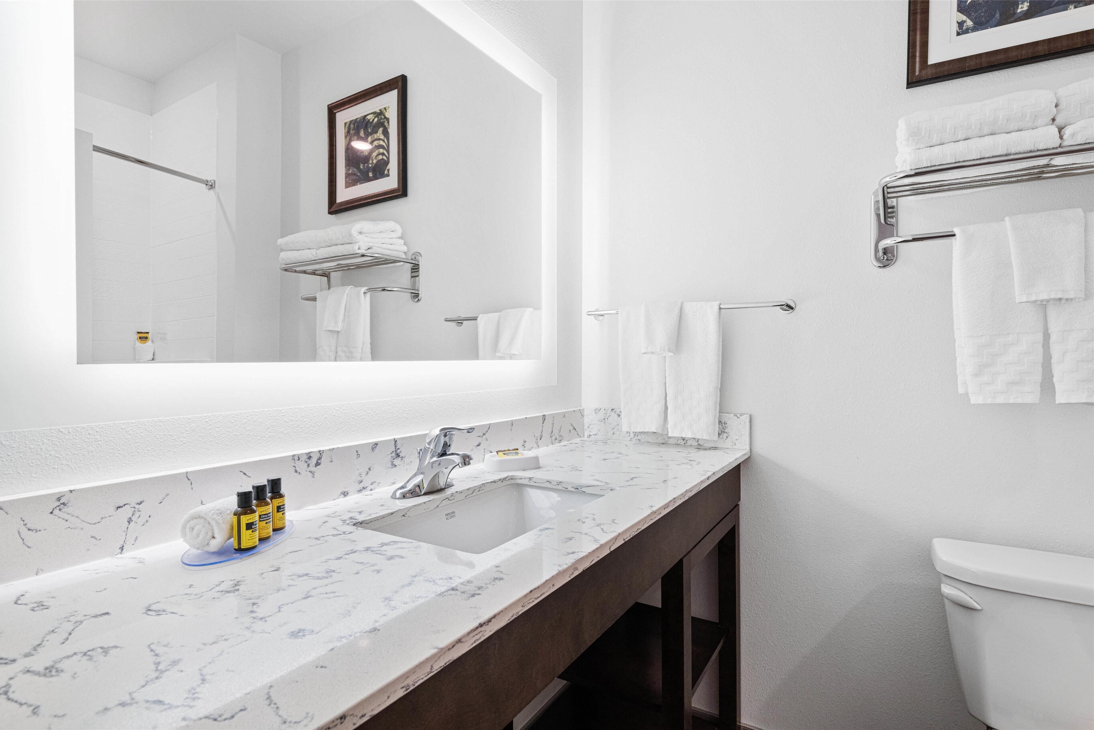 A modern bathroom with a large mirror, white sink, and a towel rack.