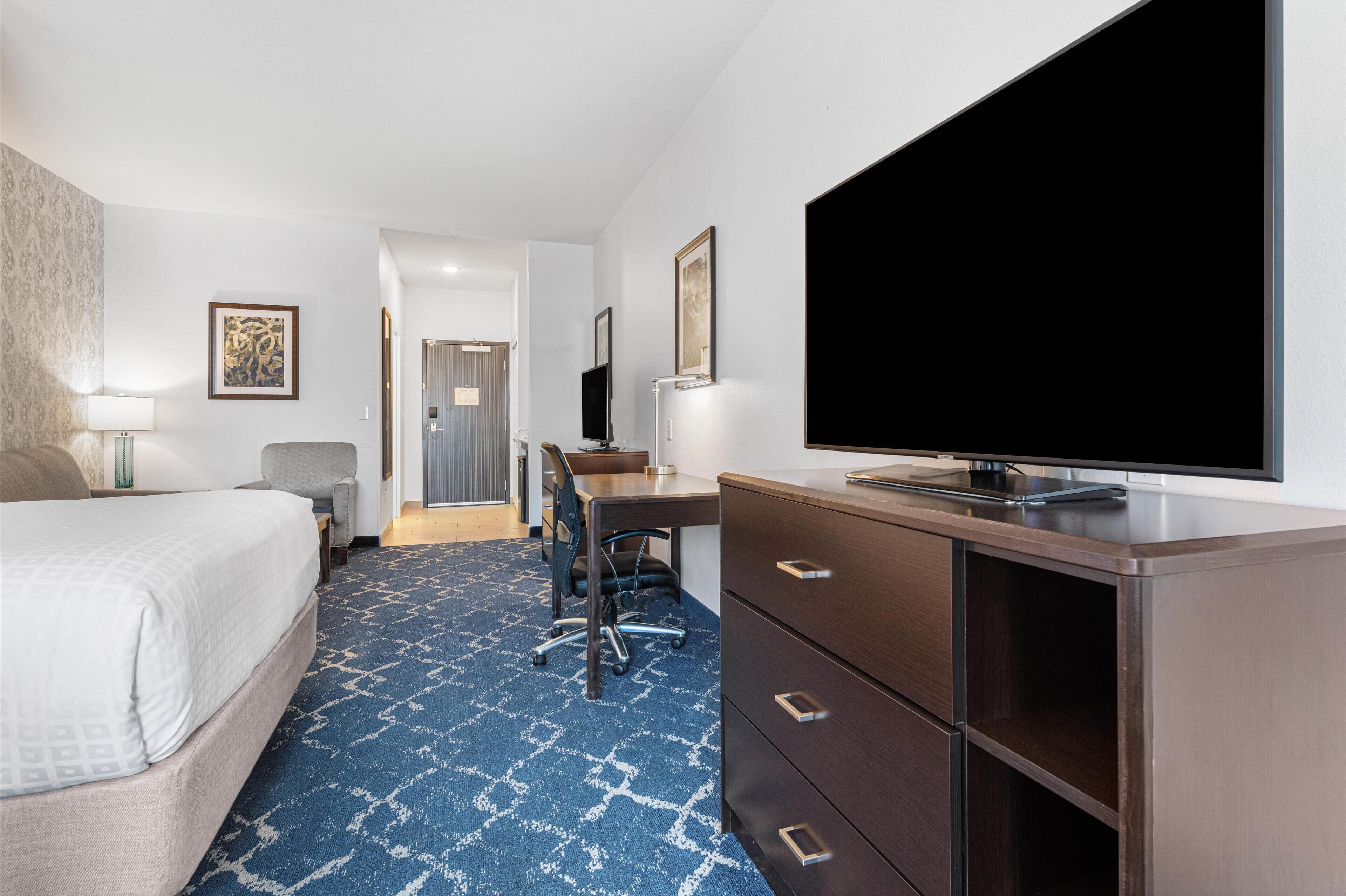 Ein Hotelzimmer mit Bett, Schreibtisch, Stuhl, Fernseher und einem großen Fenster.