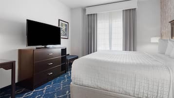 Habitación de hotel con una cama grande, un televisor de pantalla plana sobre un tocador de madera, un escritorio y una ventana con cortinas.