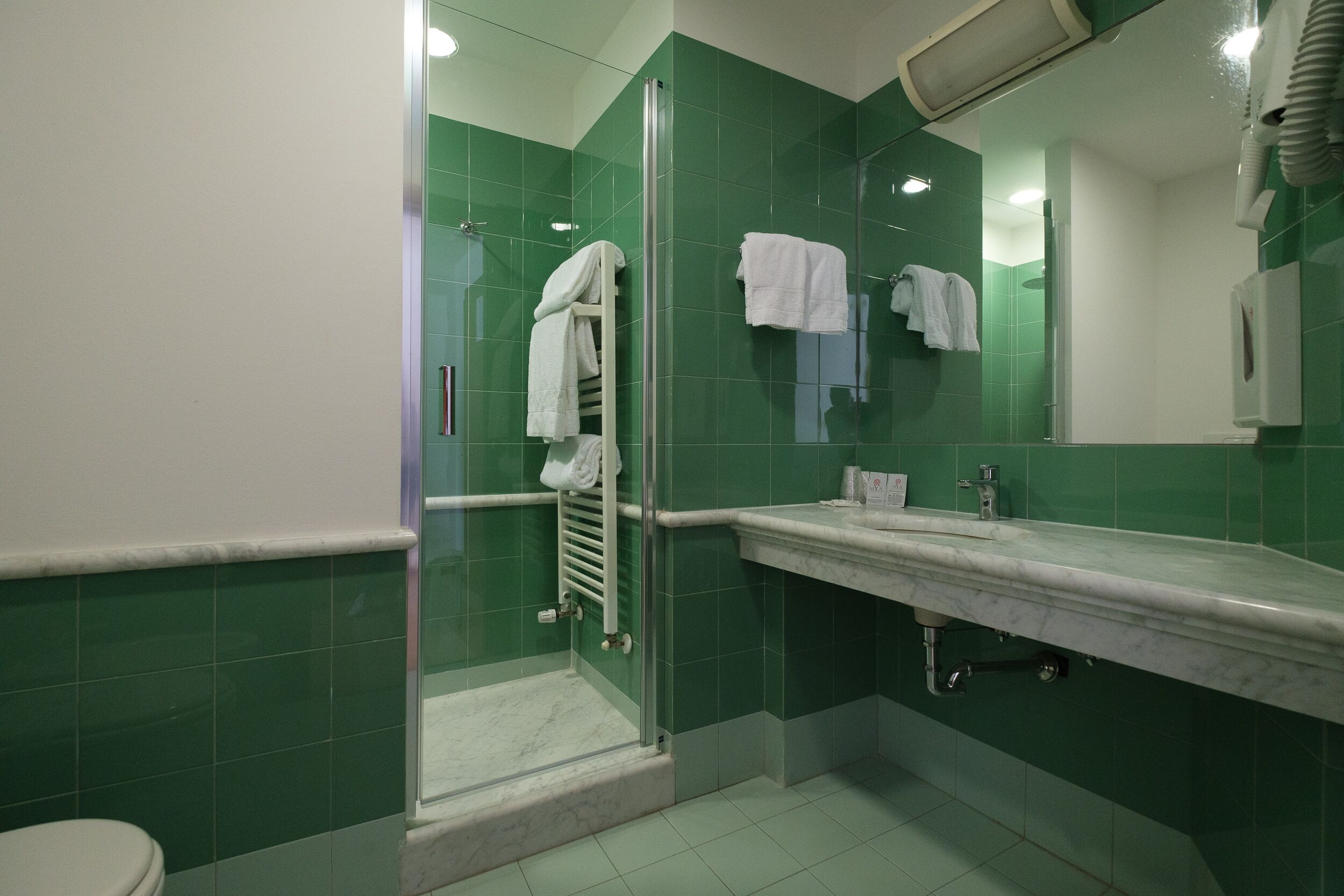 A modern bathroom with green tiles, a glass shower enclosure, a white sink, and a mirror.