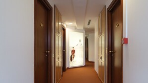 A hotel corridor with wooden doors, a brown carpet, and a white wall. - Hotel Portavaldera (Peccioli)