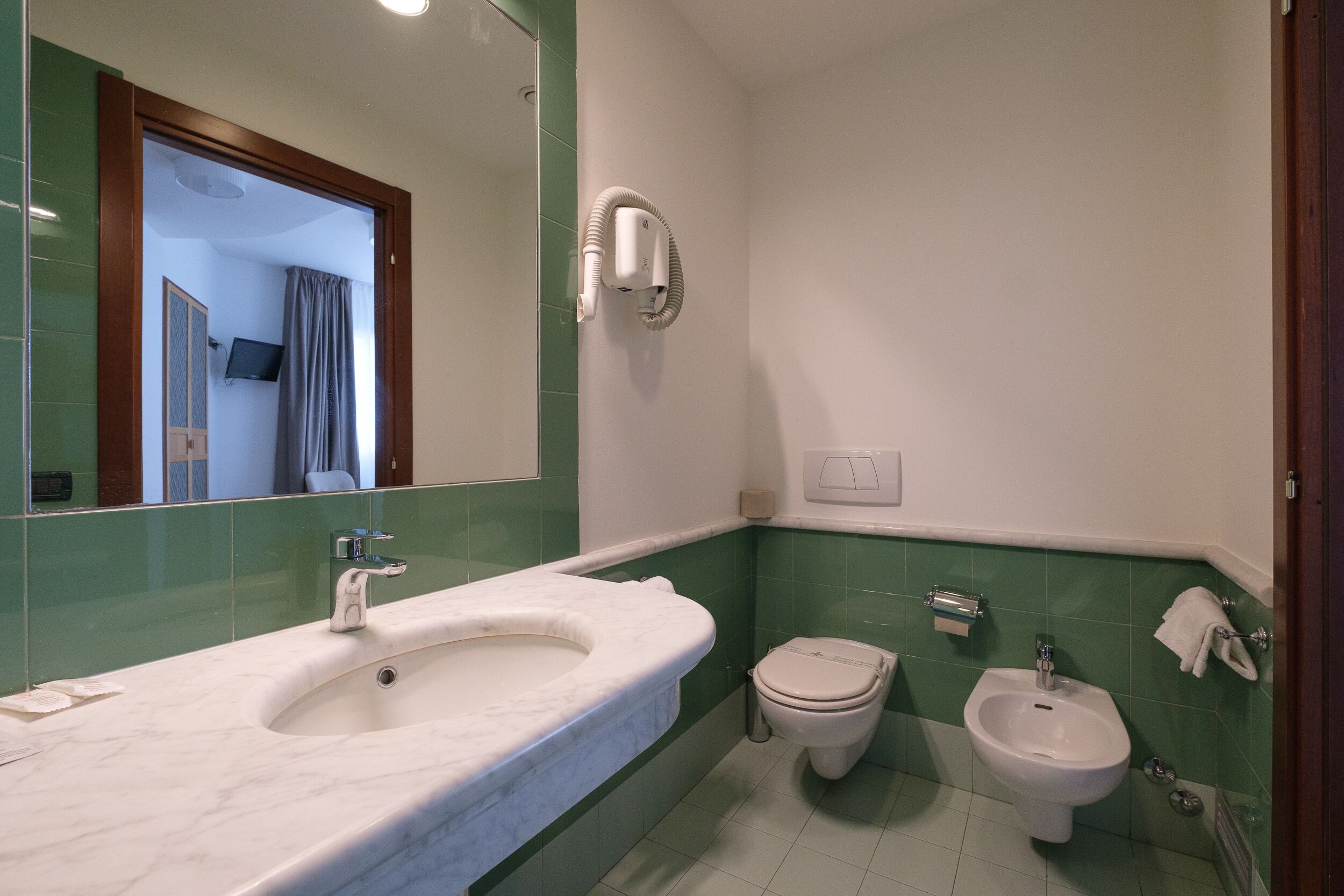Un baño con lavamanos de mármol, inodoro, bidé y espejo.