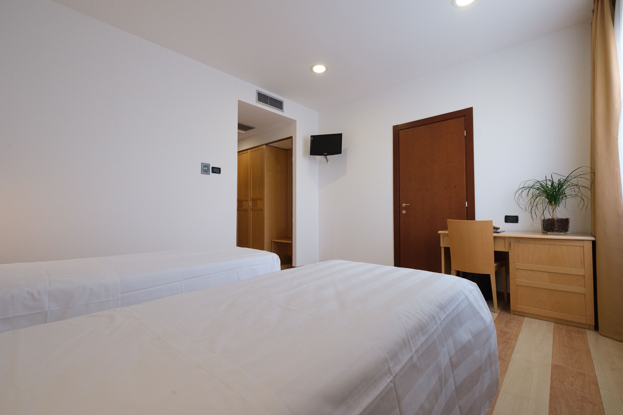 A hotel room with two single beds, a desk with a chair, a television, and a wooden wardrobe.