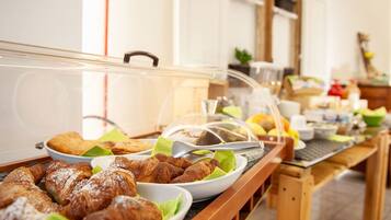 Ein Buffet mit verschiedenen Gebäcken und Speisen, darunter Croissants und einer Auswahl an Früchten.