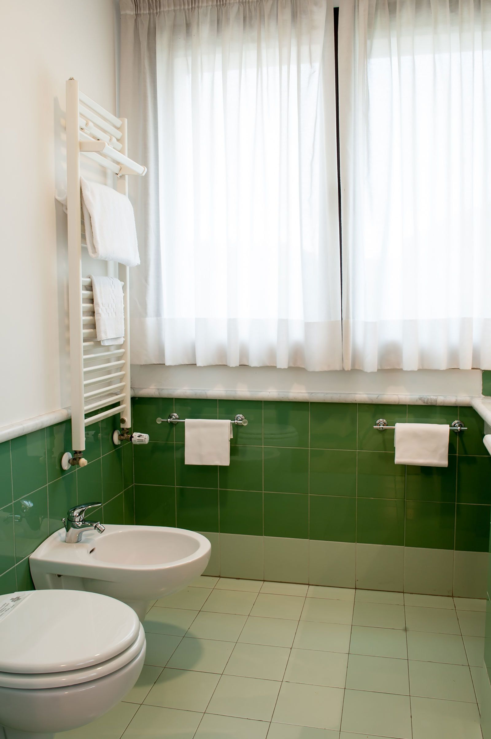 A bathroom with a green tiled wall, a white sink, a bidet, and a toilet.