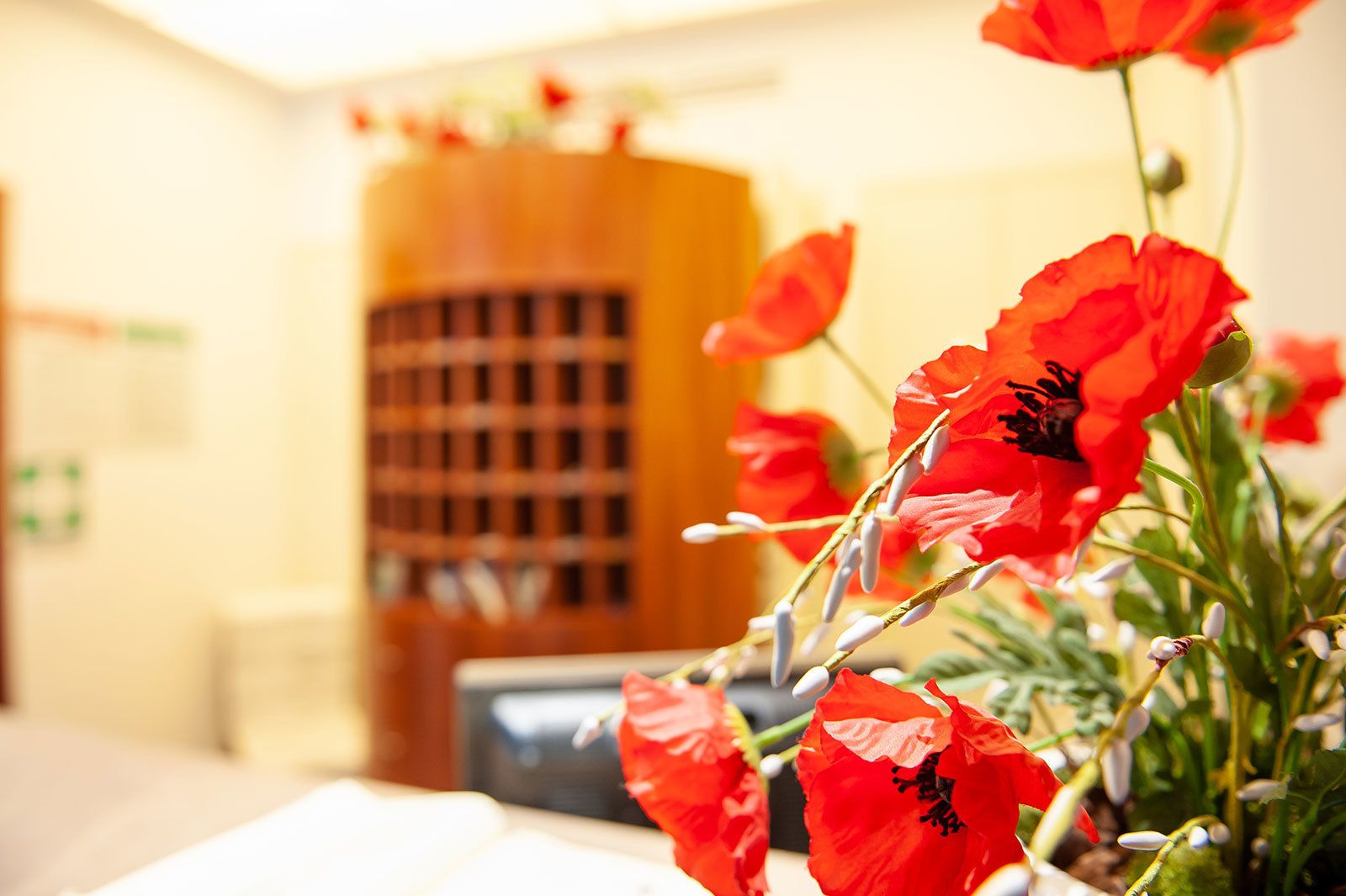 Una habitación con un armario de madera y una mesa con flores rojas.