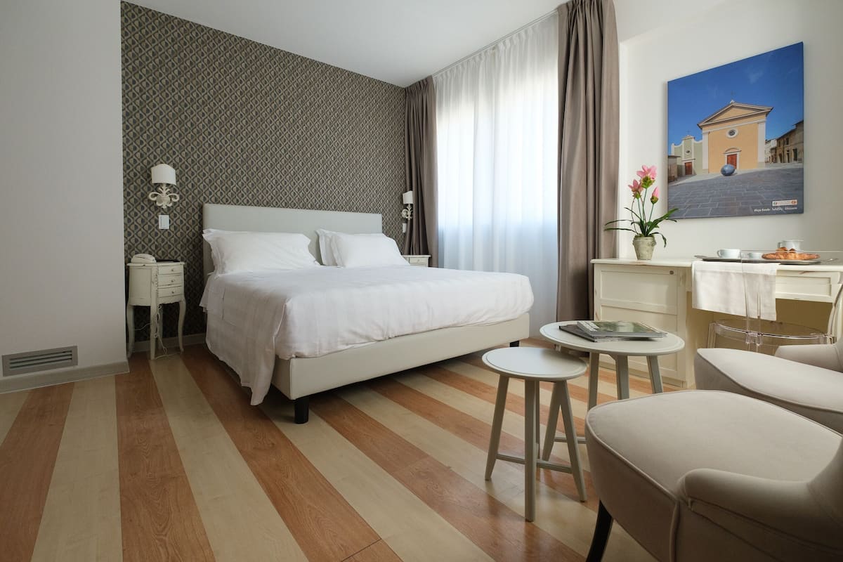A hotel room with a large bed, a desk with a chair, a small round table, and a painting on the wall.