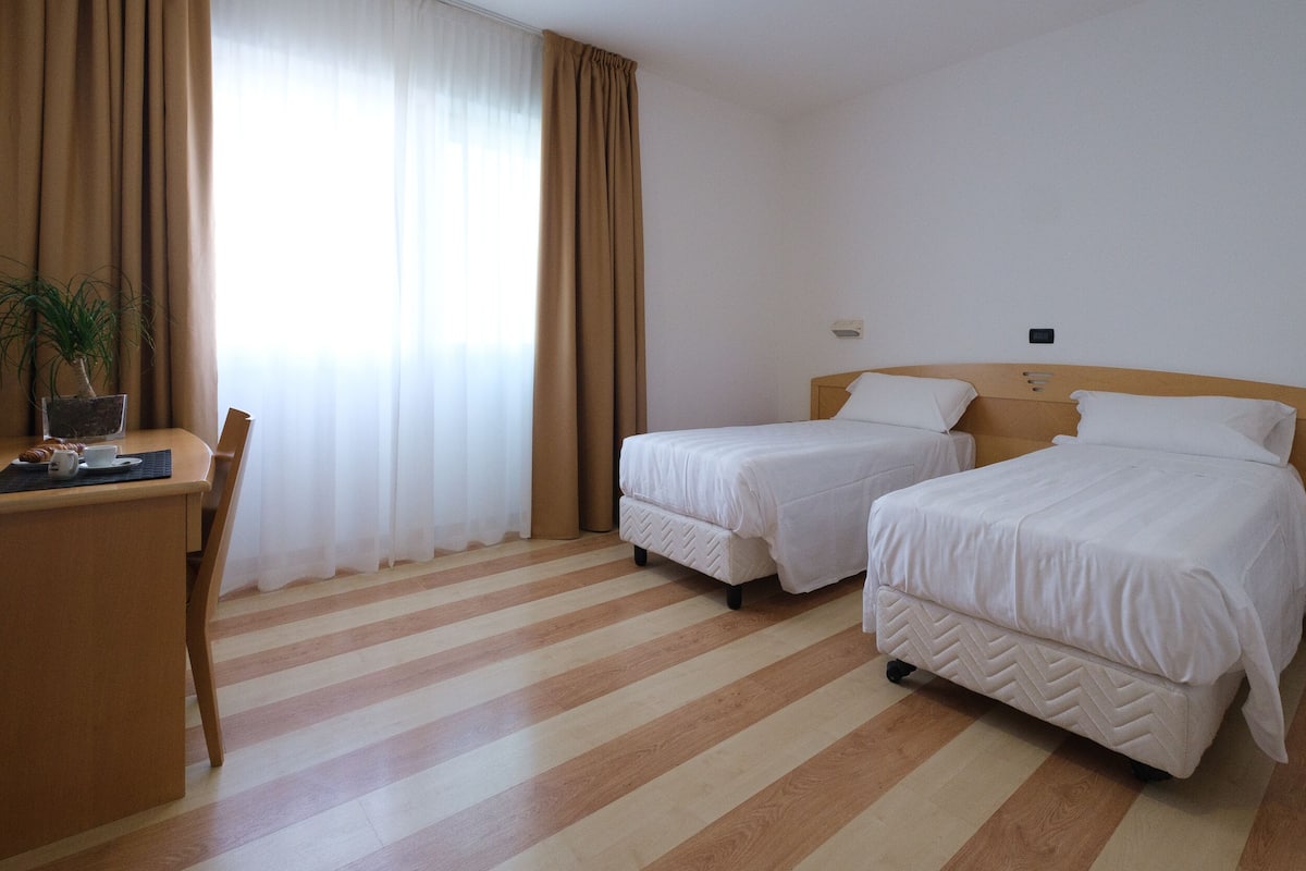 A hotel room with two single beds, a desk with a chair, and a potted plant.