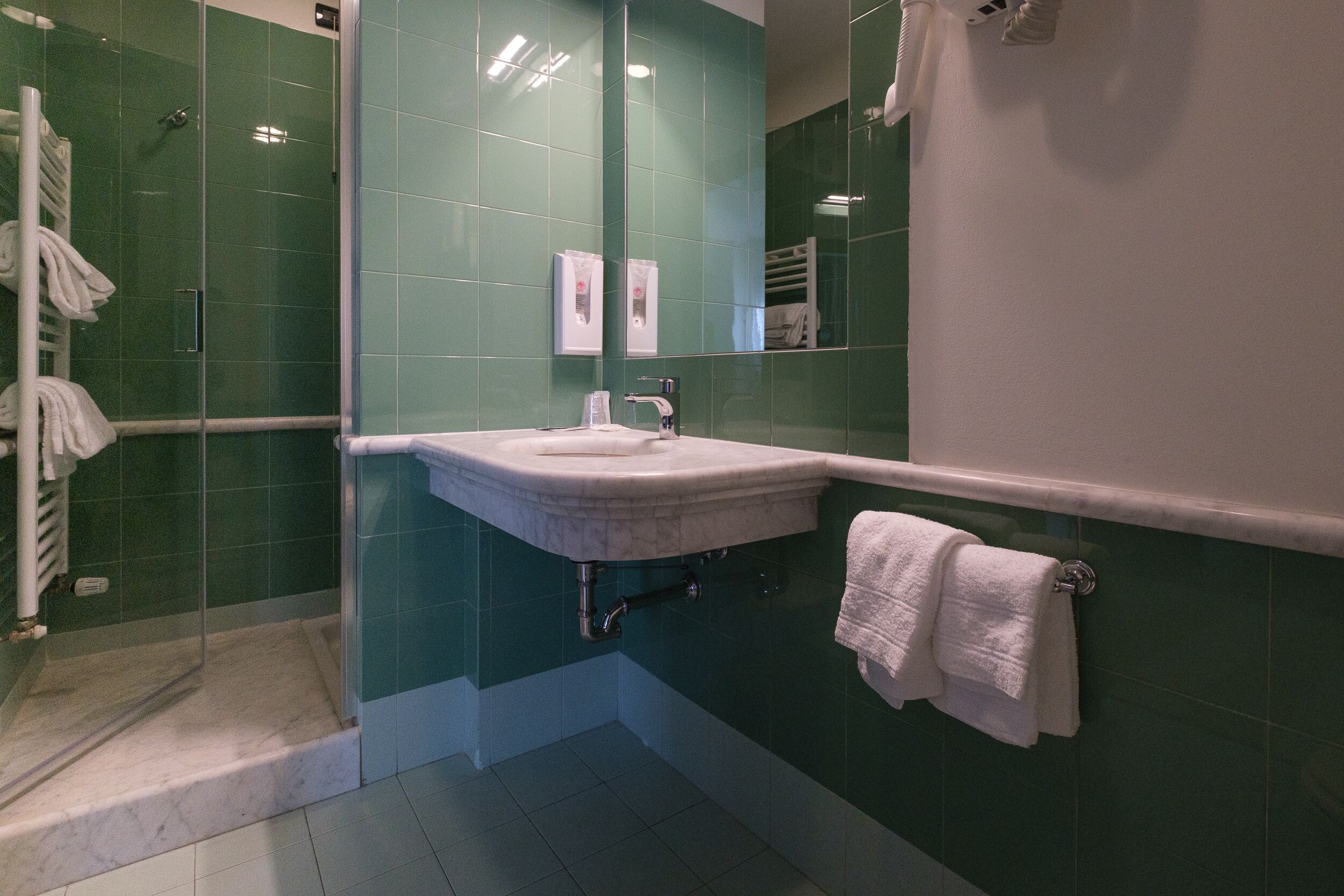 A bathroom with a glass shower enclosure, a sink with a mirror, and a towel rack.