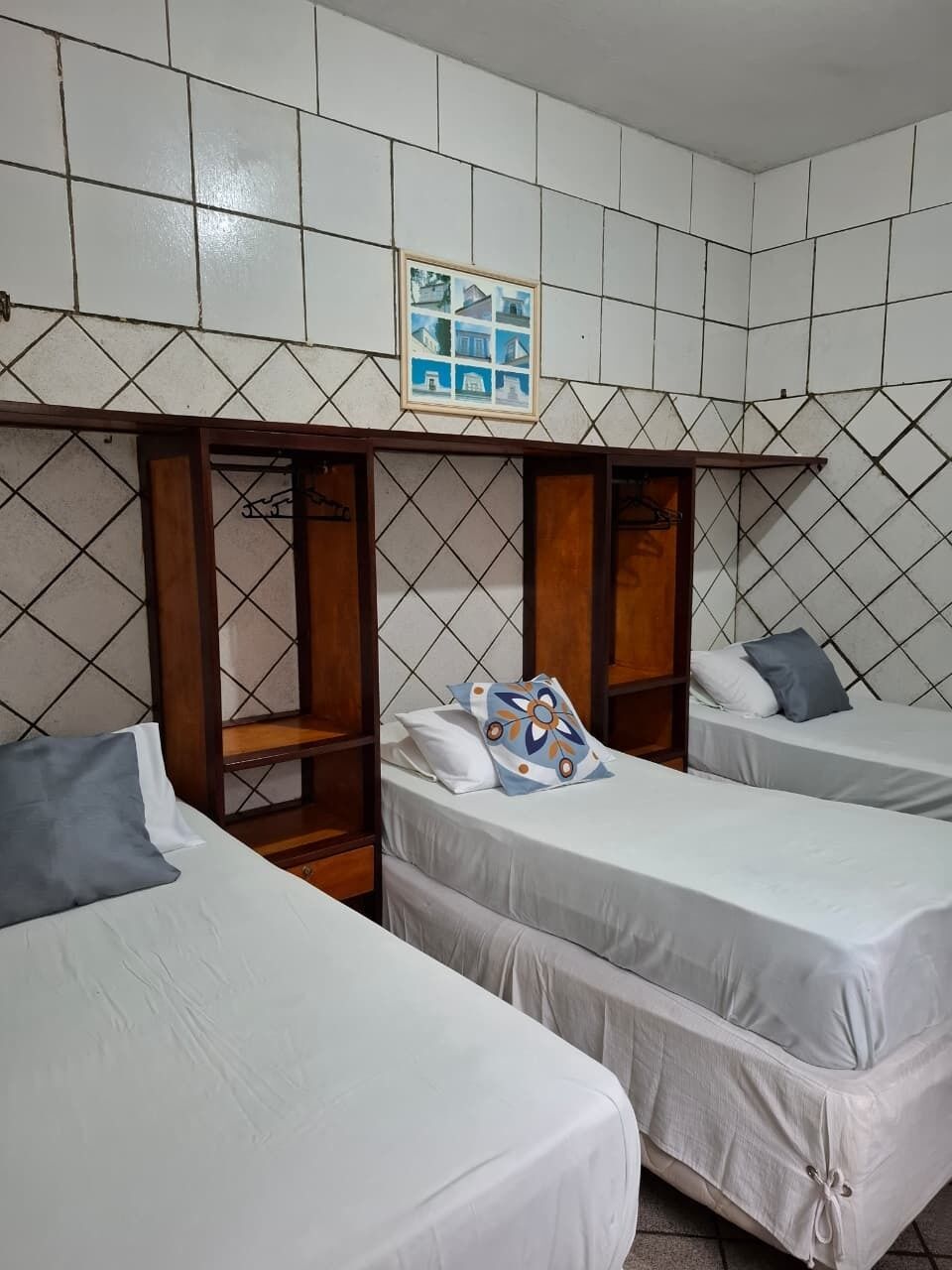 A room with two beds, a wooden shelf unit, and a framed picture on the wall.