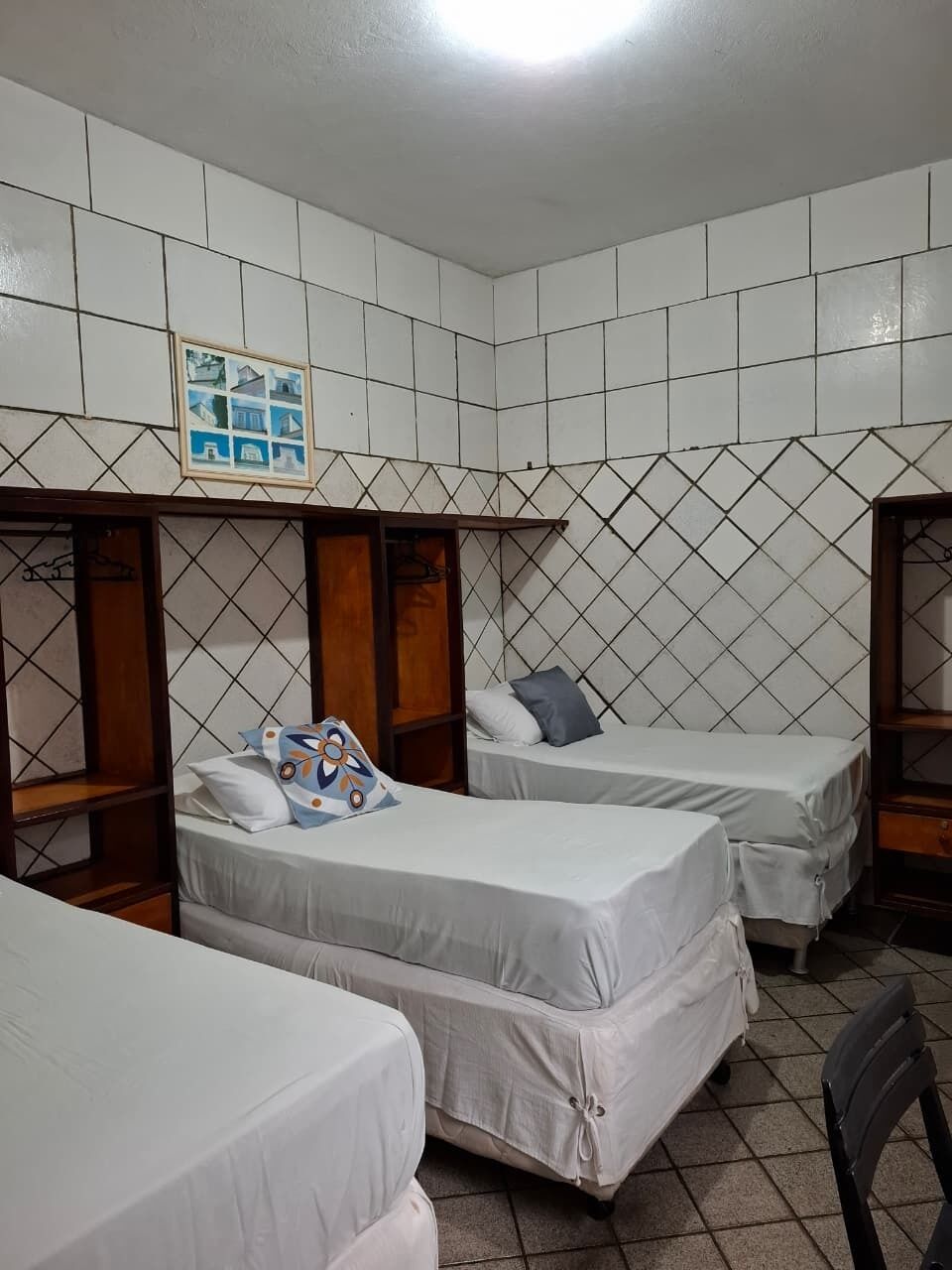 Una habitación con tres camas, un armario de madera y un cuadro enmarcado en la pared.