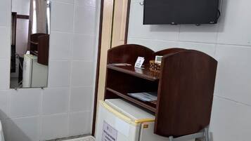 A small room with a bed, a desk with a chair, a mirror, a television, and a refrigerator.