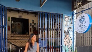 Entrada de hotel con una puerta azul, un cartel de accesibilidad para sillas de ruedas y un mural de una persona sosteniendo una bate.