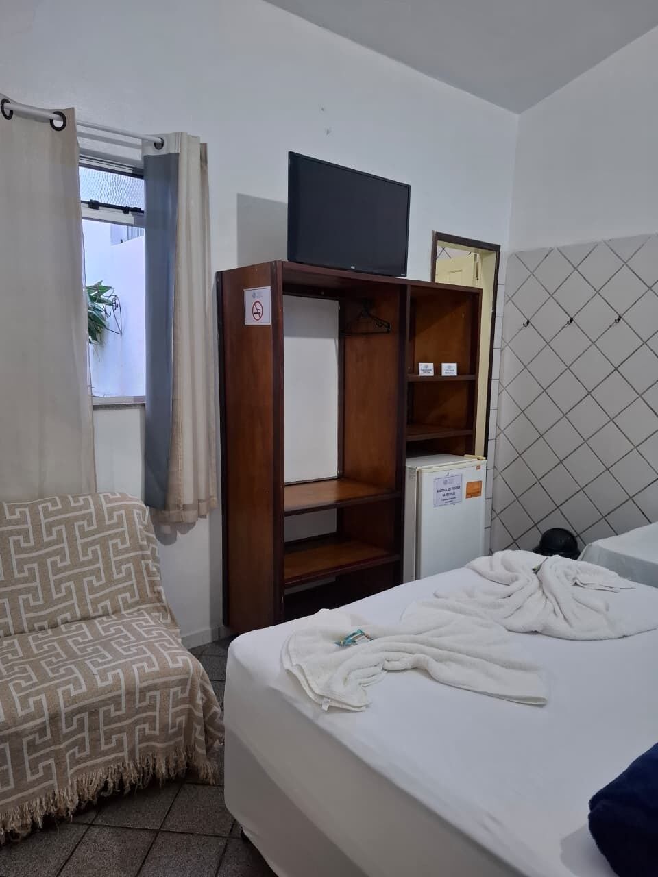 A hotel room with a bed, a wardrobe, a television, and a small refrigerator.