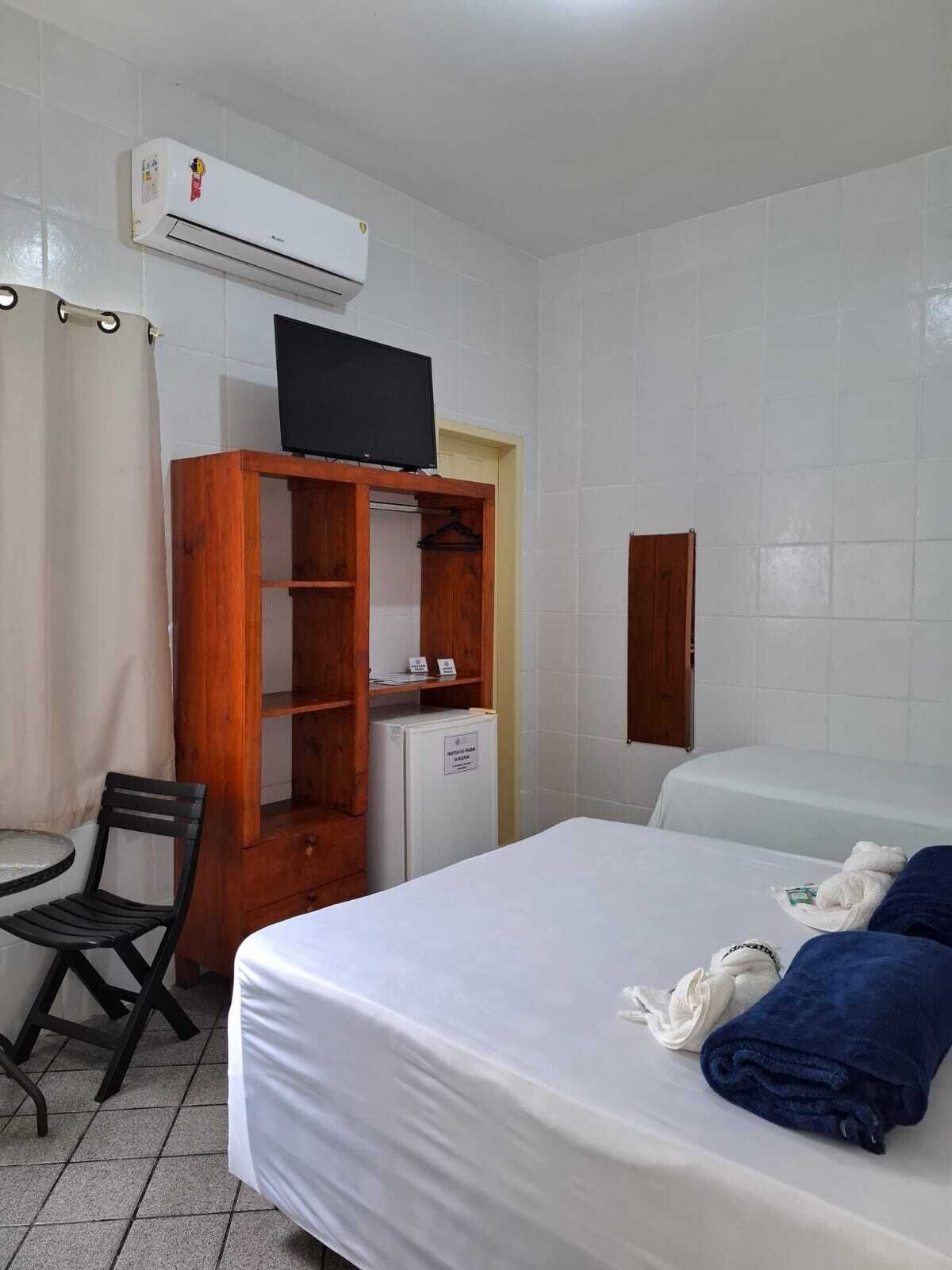 A hotel room with a bed, a wooden wardrobe, a television, a desk, and a chair.