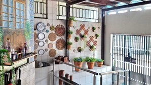 Un espacio al aire libre techado con suelo de baldosas, baranda metálica y diversas macetas con plantas.