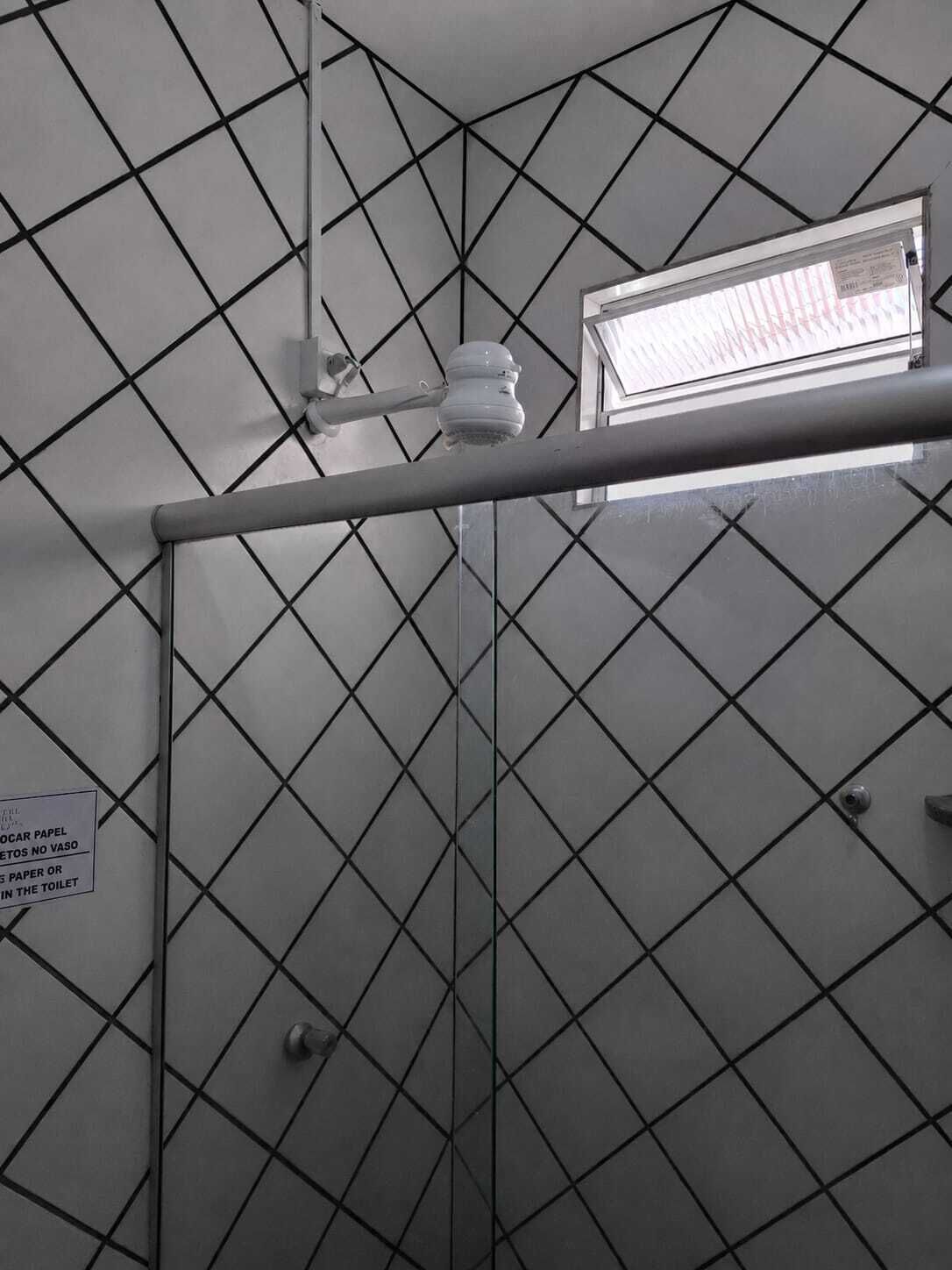A bathroom with a geometric patterned wall, a hand dryer, and a sign instructing not to flush paper or toilet paper in the toilet.