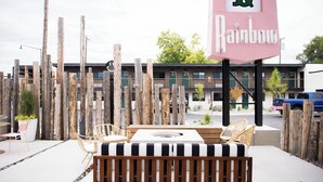 Un espace extérieur aménagé avec un banc en bois, des chaises en osier et une table agrémentée d’un coussin à rayures.
