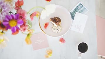 A table with a heart-shaped pastry, a cup of coffee, a postcard, and a card with a message.
