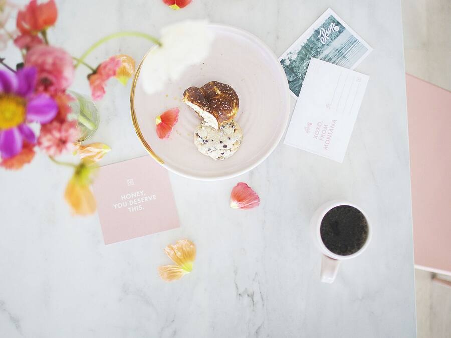 A table with a heart-shaped pastry, a cup of coffee, a postcard, and a card with a message.